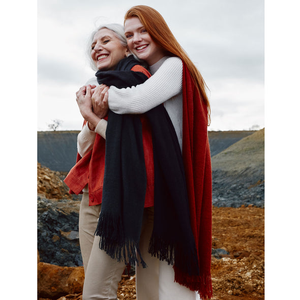 Two models, wearing scarves which have been dip dyed in subtle shades. One is dark grey to almost black and the other is rust to a deep crimson. Made from wool, yak and cashmere, these are a soft and luxurious scarf from Thread Tales company