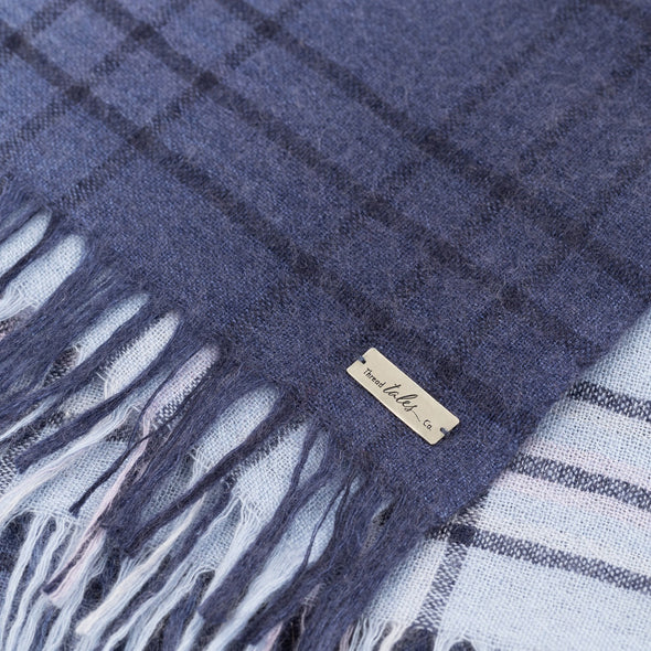 Folded detail of blue scarf woven with subtle open check in darker shade then dip dyed in shades of blue to subtle effect. Made from wool and cashmere lightweight warm luxurious scarf from Thread Tales company 