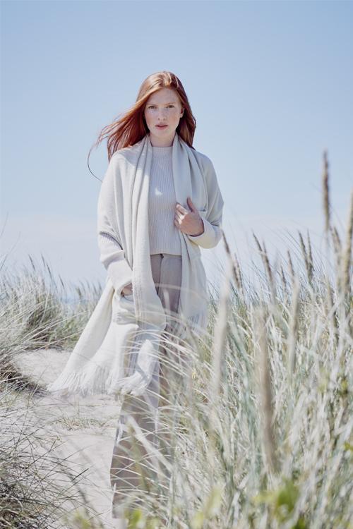 Model wearing large blanket wrap in cream Merino wool with one hand in one of the patch pockets