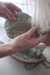Woman holding olive green Lotus silk eye mask she just removed from matching lotus silk pouch